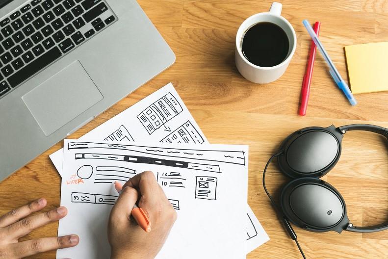 image of website planning with papers, lap top, coffee, and pens on a desk